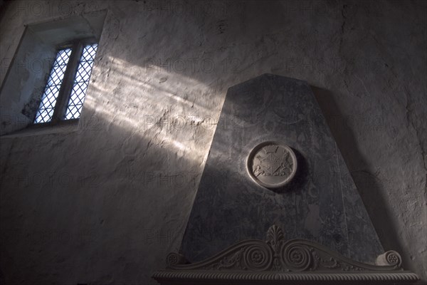 ENGLAND, West Sussex, Boxgrove, Boxgrove Priory Church of St Mary and St Blaise. Interior view of  light shining through small window onto a wall and marble monument.