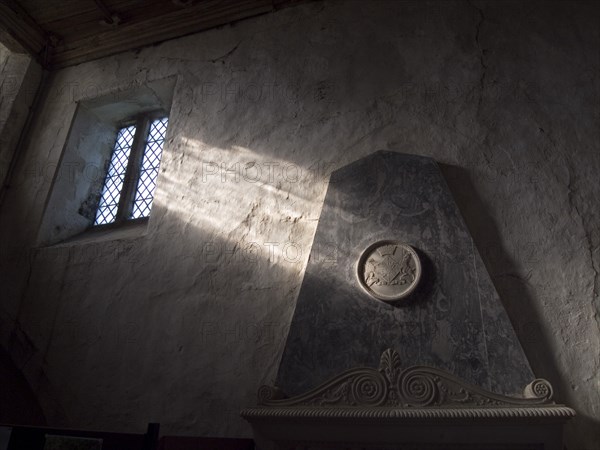 ENGLAND, West Sussex, Boxgrove, Boxgrove Priory Church of St Mary and St Blaise. Interior view of  light shining through small window onto a wall and marble monument.