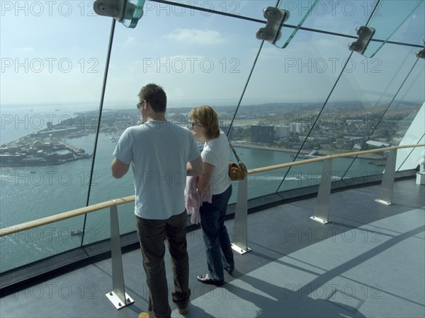 ENGLAND, Hampshire, Portsmouth, "Gunwharf Quays. The Spinnaker Tower. Interior view with visitors looking out of glass windows on the top observation deck, providing a 320° view of the city of Portsmouth, the Langstone and Portsmouth harbours, and a viewing distance of 37 kilometres (23 miles)"