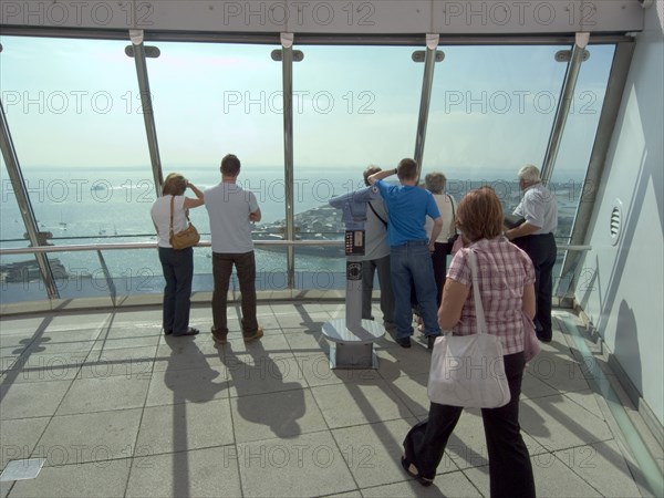 ENGLAND, Hampshire, Portsmouth, "Gunwharf Quays. The Spinnaker Tower. Interior view with visitors looking out of glass windows on the top observation deck, providing a 320° view of the city of Portsmouth, the Langstone and Portsmouth harbours, and a viewing distance of 37 kilometres (23 miles)"