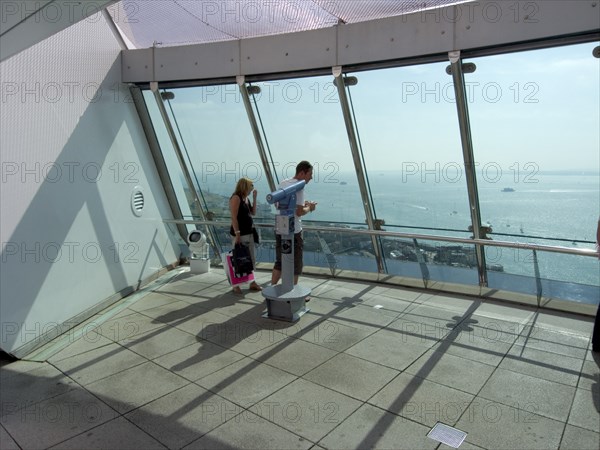 ENGLAND, Hampshire, Portsmouth, "Gunwharf Quays. The Spinnaker Tower. Interior view with visitors looking out of glass windows on the top observation deck, providing a 320° view of the city of Portsmouth, the Langstone and Portsmouth harbours, and a viewing distance of 37 kilometres (23 miles)"