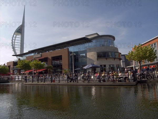ENGLAND, Hampshire, Portsmouth, "Gunwharf Quays complex. View across water towards restaurants, bars and shopping outlets. Spinnaker Tower behind."