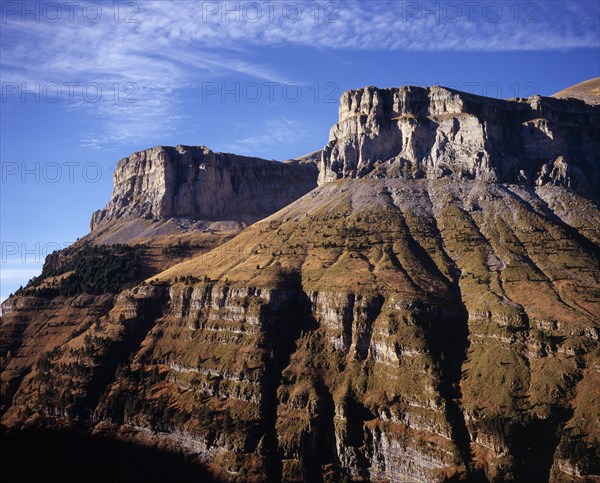 SPAIN, Aragon, Valle de Ordesa, Eroded cliffs above Bosque de Las Hayas.  Grey rock scattered with trees and partly covered with brown / green vegetation.