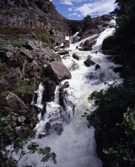 WALES, Gwynedd, Snowdonia National Park, Ogwen Falls and Nant Ffrancon Pass.   White foaming water tumbling over rocks with arched stone bridge in background.