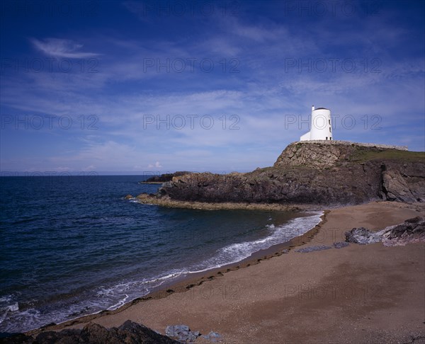 WALES, Isle of Anglesey, Llanddwyn Island, "Curving, empty beach overlooked by old lighthouse standing on rocks extending out to sea.  Blue sky and windswept clouds above."
