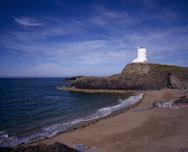 WALES, Isle of Anglesey, Llanddwyn Island, "Curving, empty beach overlooked by old lighthouse standing on rocks extending out to sea. Blue sky and windswept clouds above."