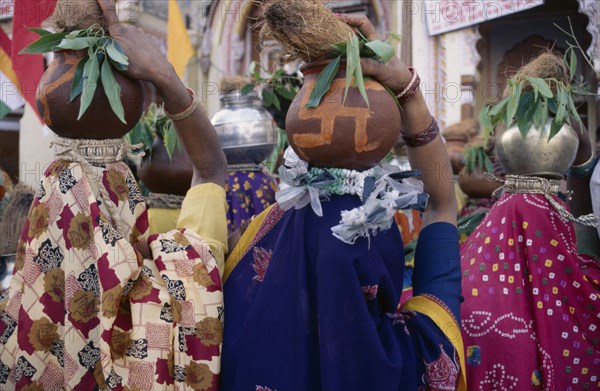 INDIA, Madhya Pradesh, Orccha, Back view of crowd of women carrying metal and earthenware pots on their heads with offerings of coconuts.