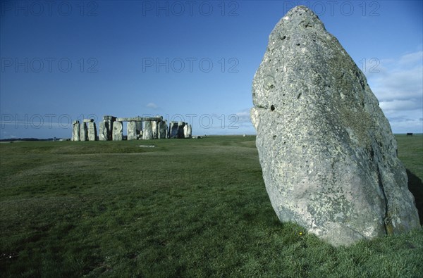 ENGLAND, Wiltshire, Stonehenge, View across the grass on Salisbury Plain toward the standing stones with a large stone in the foreground