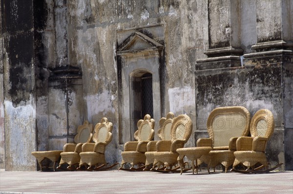 NICARAGUA, Leon, "Street scene with line of wicker chairs and tables outside building with crumbling, discoloured plaster wall."