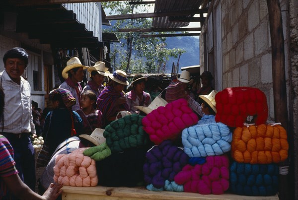 GUATEMALA, Todos Santos, Market scene with wool stall piled with brightly coloured bundles of wool and crowd of customers wearing traditional dress.