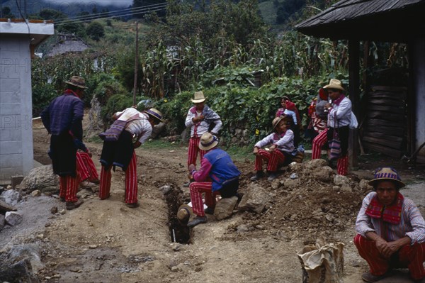 GUATEMALA, Todos Santos, "Group of men wearing traditional dress looking at recently dug drainage channel, maize, squash and fruit trees behind."