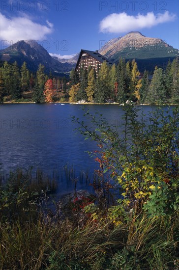 SLOVAKIA, Carpathian Mtns, High Tatras Mtns, Strbske Pleso.  View across lake towards chalet and mountains beyond with surrounding trees and vegetation in Autumn colours.