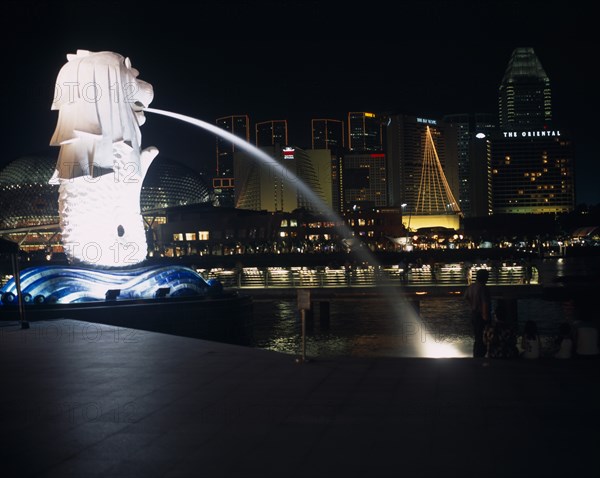 SINGAPORE, Merlion Park, "The Merlion statue at the Merlion Park river entrance at night with the esplanade concert hall, Oriental Hotel and other city buildings illuminated behind."