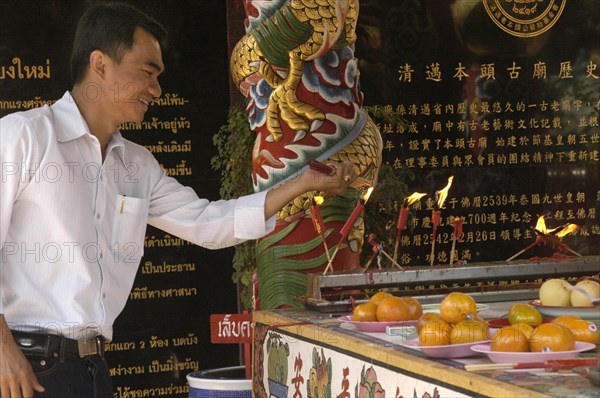 THAILAND, North, Chiang Mai, "Chinese New Year celebrations. A worshiper lighting joss sticks at a Chinese temple, Warorot Market, Chiang Mai's China Town,"