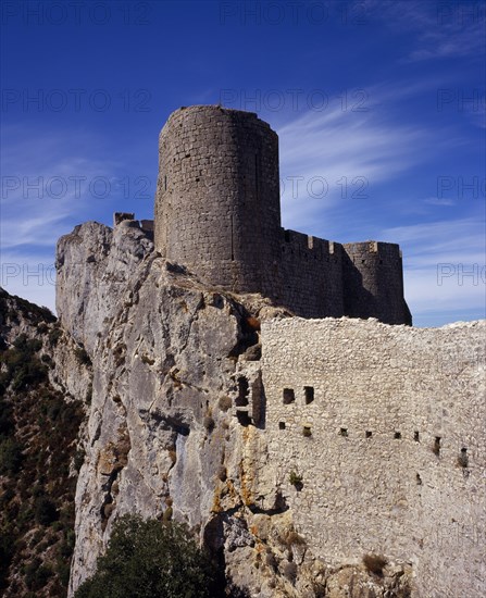 FRANCE, Languedoc-Roussillon, Aude, "Chateau Peyrepertuse.  Ruined medieval Cathar castle stronghold, outer tower of the governor’s quarters rising above fortified walls set into limestone rock."