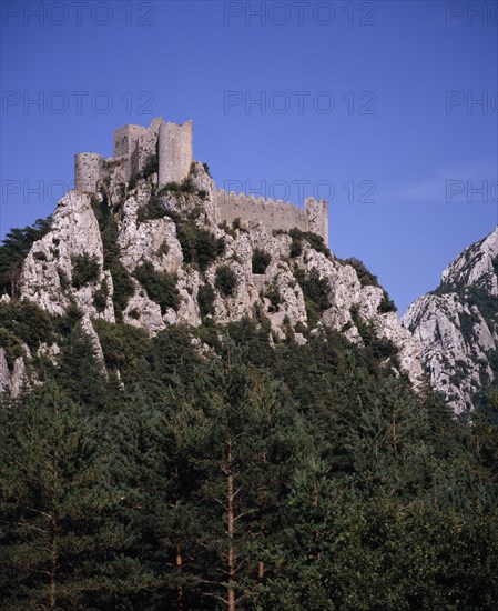 FRANCE, Languedoc-Roussillon, Aude, Chateau Puilarens.  Ruined medieval Cathar castle stronghold set high on limestone cliff showing keep.  With trees at foot of cliff in foreground.
