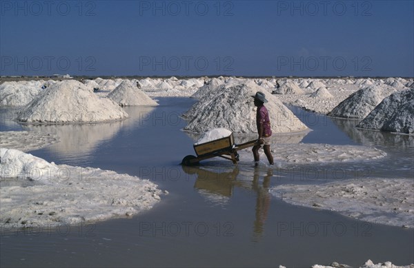 COLOMBIA, La Guajira , Manaure, Manaure Salt Mines in the Guajira Peninsula. A worker pushing a wheel barrow load of salt through the salt pans to trucks which transport the salt throughout Colombia.