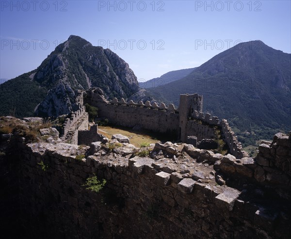 FRANCE, Languedoc-Roussillon, Aude, Chateau Puilarens.  Ruined medieval Cathar castle stronghold set high on limestone cliff.  View looking down on battlements from the keep to mountain peaks beyond.