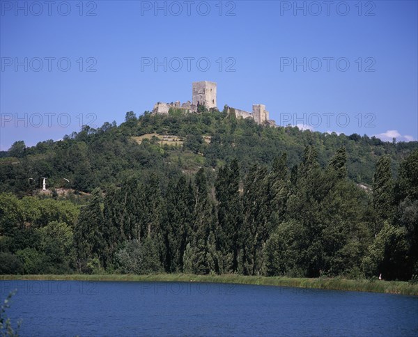 FRANCE, Languedoc-Roussillon, Aude, "Chateau Puivert, view from south high on wooded hillside above village and its lake.  Cathar castle stronghold during war with the Catholic church in the 13th century."