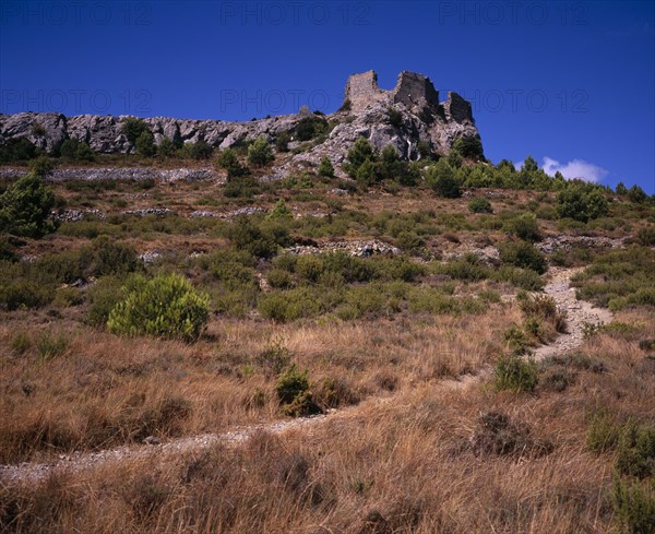 FRANCE, Languedoc-Roussillon, Aude, "Ruins of Chateau Perillos east of Tuchan situated on hillside with scattered outcrops of rock and windswept vegetation and narrow, stony track in foreground."