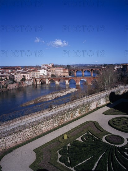 FRANCE, Midi-Pyrenees, Tarn, Albi.  View across town over gravel paths and clipped hedges of Bishop’s Gardens towards bridges spanning the River Tarn.