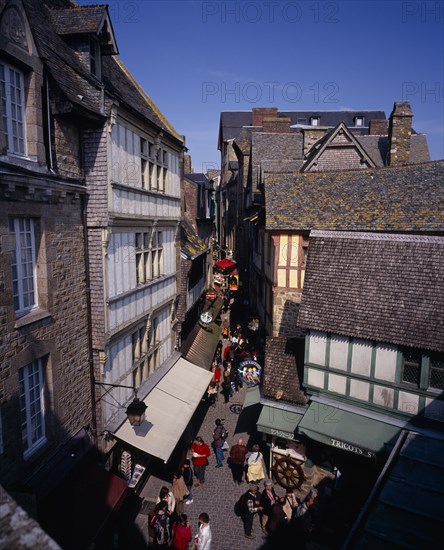 FRANCE, Normandy, Mont-St-Michel, "Looking down on narrow street, souvenir arcade and shoppers from outer wall footway."
