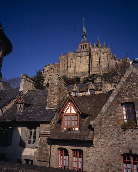 FRANCE, Normandy, Mont-St-Michel, The Abbey on hilltop above tiled rooftops of town houses from the Archade Tower.