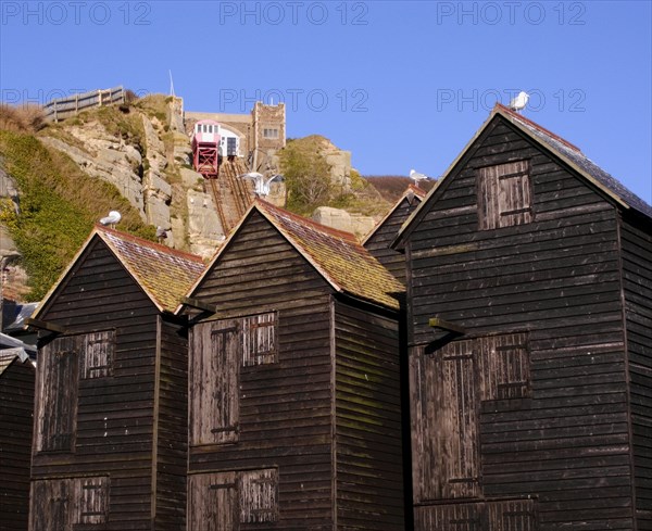 ENGLAND, East Sussex, Hastings, Black wooden huts used for storing fishing nets.The East Hill Lift funicular railway behind.