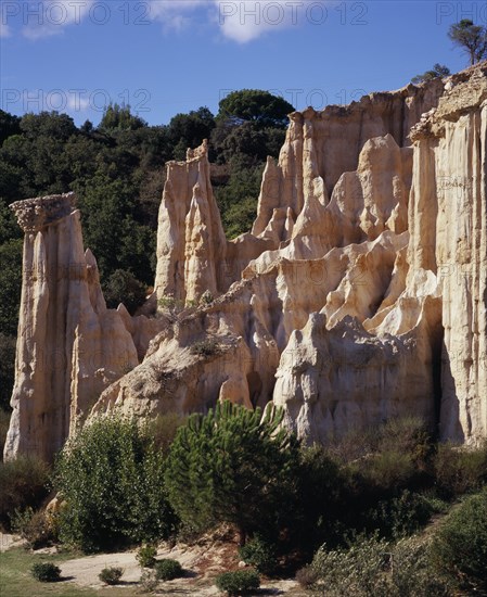FRANCE, Languedoc-Roussillon, Pyrenees-Orientales, Ille Sur Tet.  Sandstone area known as Orgues.  Eroded sandstone cliff formed into pinnacles rising above shrubs and trees with tree covered hillside behind.