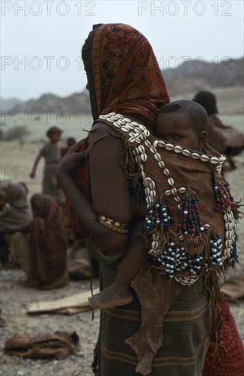 ETHIOPIA, Danakil , People, Mother carrying baby on her back in leather sling decorated with beads and cowrie shells.