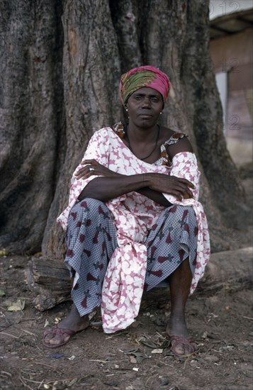 SENEGAL, People, Portrait of woman seated at base of tree trunk wearing fabric of different printed patterns.