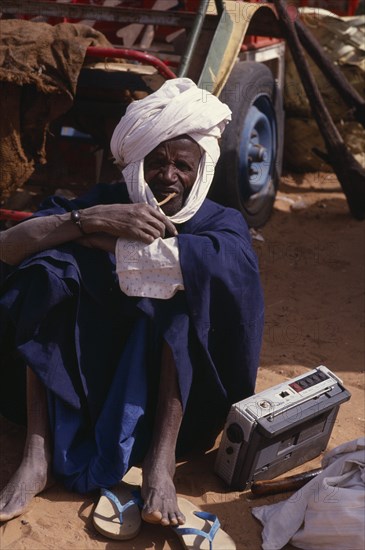 SENEGAL, People, Portrait of Senegalese man seated on ground listening to radio.