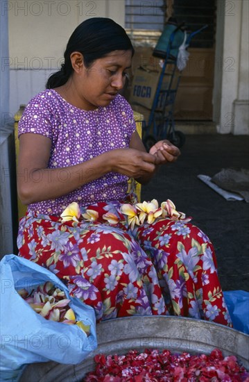 MEXICO, Juchitan, Woman in floral patterned skirt threading flower heads into garland at Juchitan street market.