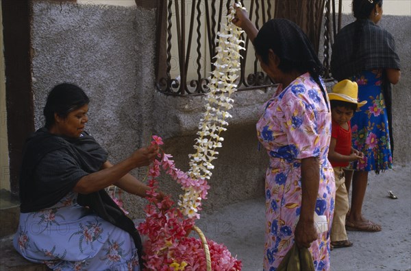 MEXICO, Guerrero, Woman vendor and customer at flower market stall looking at frangipani flower garlands.