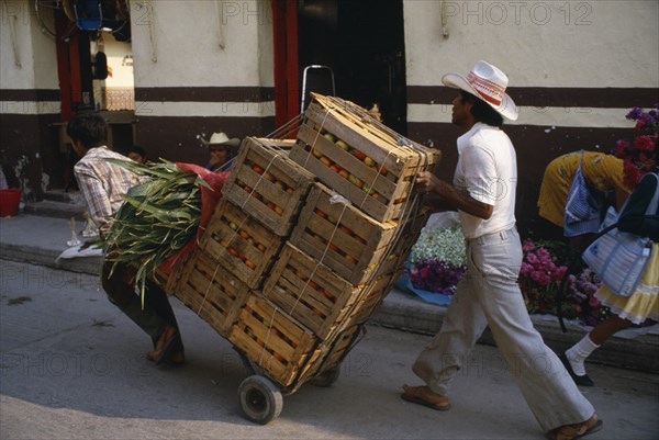 MEXICO, Guerrero State, Work, Traders using sack truck to transport wooden crates of fruit through street.