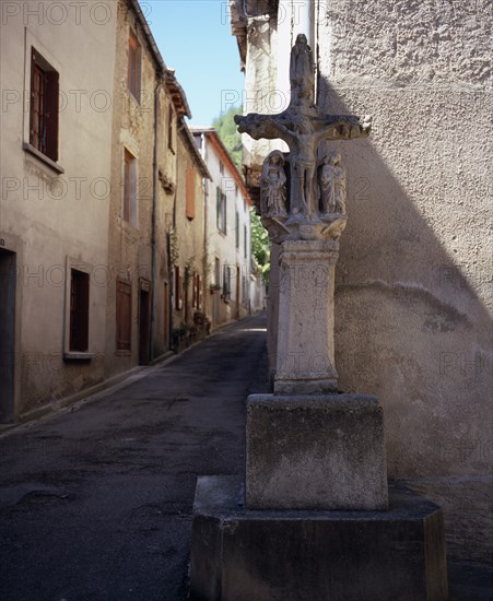FRANCE, Languedoc-Roussillon, Aude, Mas-Cabardes.  Village street corner with Croix de la Tisserands or the Weaver’s Cross standing against wall.