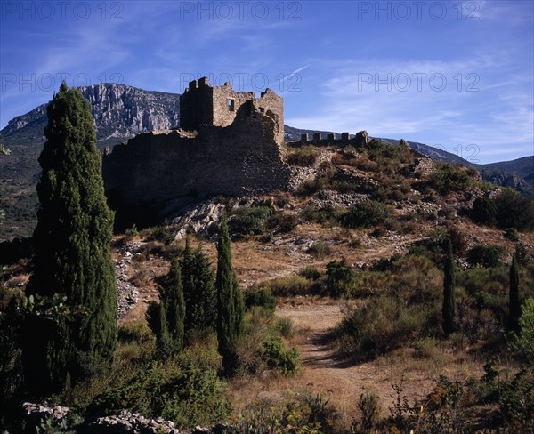 FRANCE, Languedoc-Roussillon, Aude, "Chateau Padern.  Ruined fortifications perched on steep, rocky hillside above village amongst cypress trees with mountain backdrop."