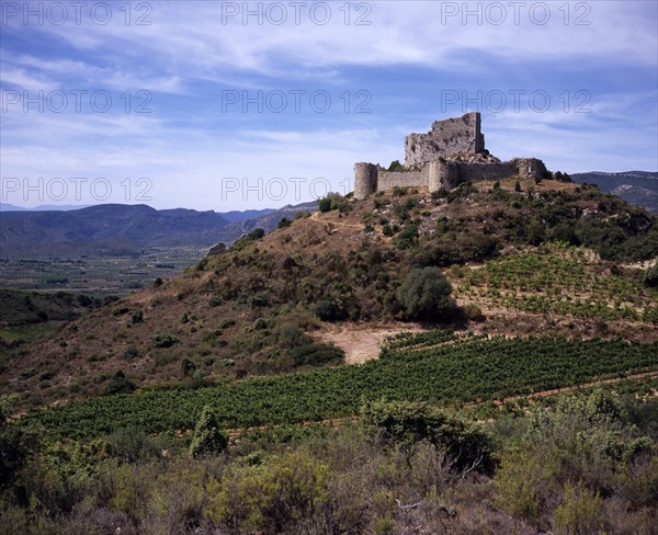 FRANCE, Languedoc-Roussillon, Aude, Chateau de Aguilar.  Ruins of twelth Century Cathar castle set on hillside in the commune of Tuchan.  Inner keep surrounded by outer thirteenth century fortification. Vines growing in valley below.