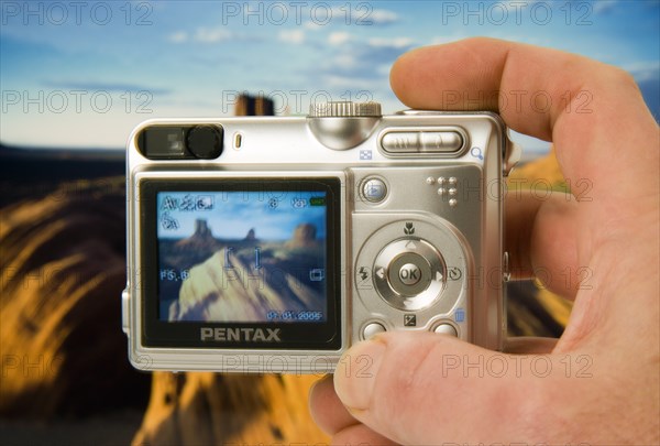 TECHNOLOGY, Media, Photography, Digital camera held in a hand with an image on the screen and in the background of Monument Vally (studio shot with camera held in front of a print)