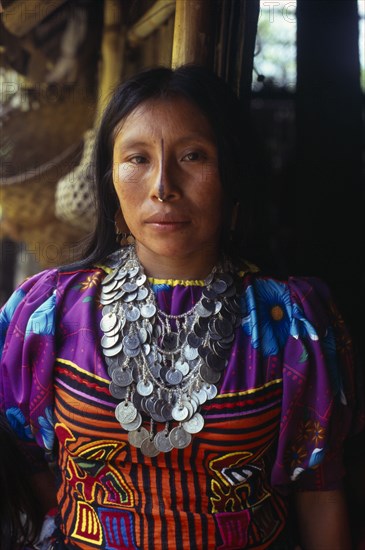 COLOMBIA, Darien, Kuna Indigenous Tribe, Three-quarter portrait of Kuna Indian woman from the Arquia community wearing traditional Mola applique layered design of mythical Kuna birds  gold nose ring with black line drawn along length of nose and a silver necklace of old Colombian and Panamanian coins. Cuna