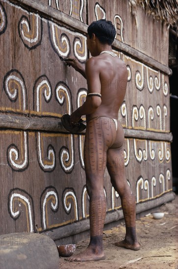 COLOMBIA, North West Amazon, Tukano Indigenous Tribe, "Barasana man (sub group of Tukano) with We body paint, white glass bead necklace  forest seed elbow bands  painting the front of maloca with white and yellow clays and black charcoal for festival "