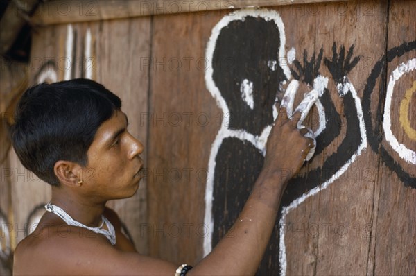 COLOMBIA, North West Amazon, Tukano Indigenous Tribe, Barasana man (sub group of Tukano) paints front of maloca large communal home. The symbolic shamanic figure is to keep evil spirits and bad weather away.