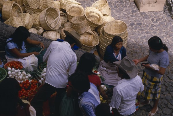 MEXICO, Taxco, Looking down on customers at fruit and vegetable stall in market with piled baskets behind.