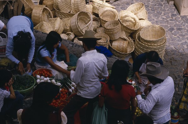 MEXICO, Taxco, Looking down on customers at fruit and vegetable stall in market with woven baskets piled behind.