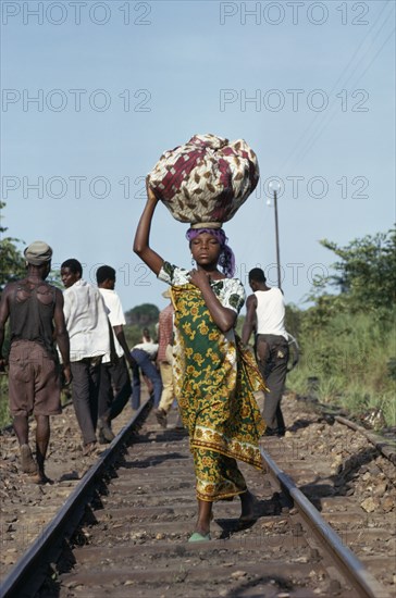 CONGO, Shaba Province, People, Young woman dressed in traditional local textiles carrying bundle on her head as she walks along railway track to market.