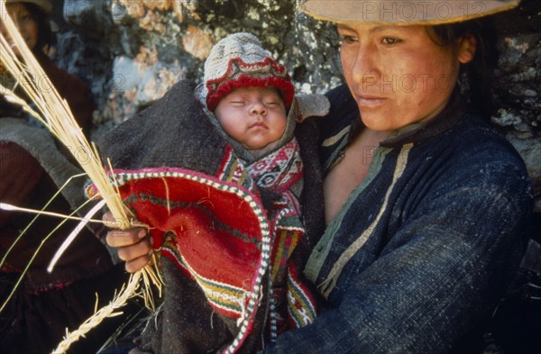 20088960 PERU  Apurimac Gorge Woman carrying baby while weaving or trensing ichu grass used in construction of traditional bridge and built by local villagers near the Rio Apurimac.