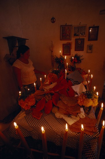 MEXICO, Acatlan, Woman lighting candles around altar for Day of the Dead covered with food and flowers.