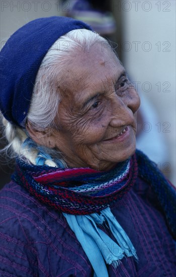 MEXICO, Oaxaca, Juchitan, Matriarchal society.  Head and shoulders portrait of elderly woman with white hair wearing purple dress and blue headscarf.