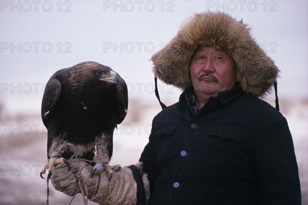 20088819 CHINA Xinjiang Province People Kazakh man wearing thick fur lined hat and holding eagle on his gloved hand.