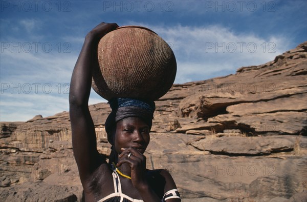 20088755 MALI Pays Dogon People Dogon woman carrying clay pot of beer on her head to nearby village.